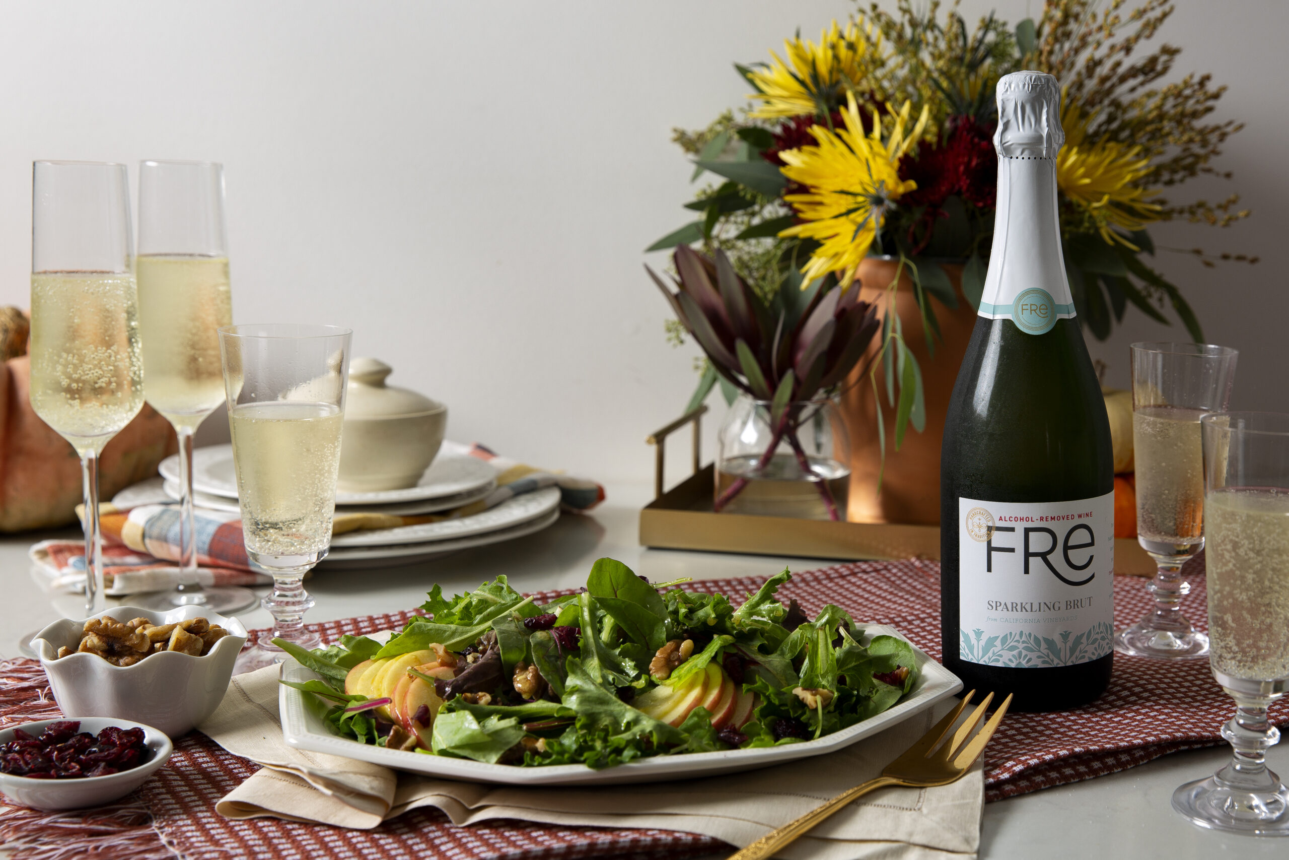 Plate of apple, walnut and mixed greens salad on a table with champagne flutes and a bottle of FRE alcohol-removed Sparkling Brut