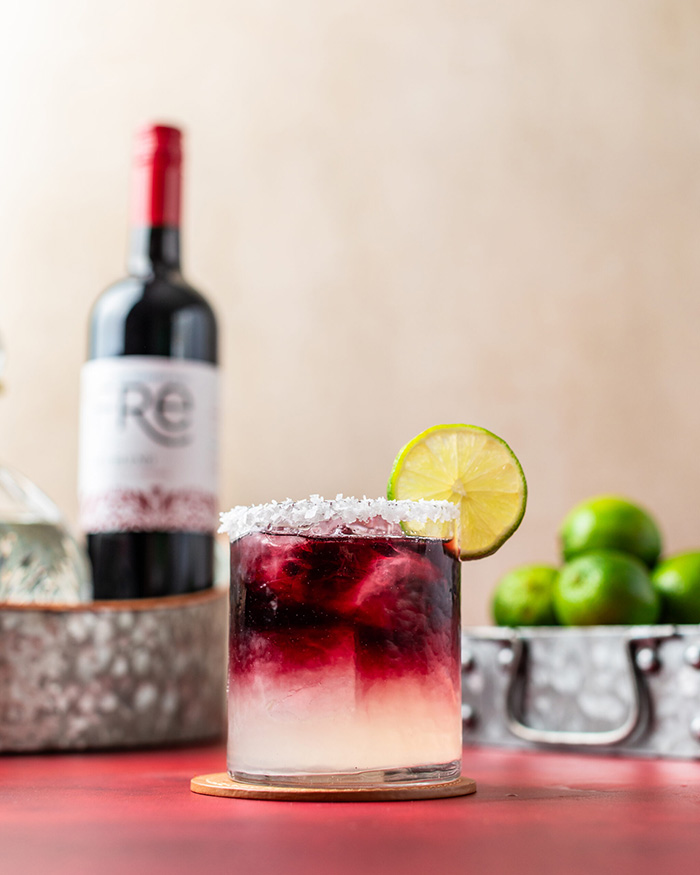 color image of a bottle of FRE Alcohol-Removed wine with a dark red and white cocktail with a lime wheel garnish