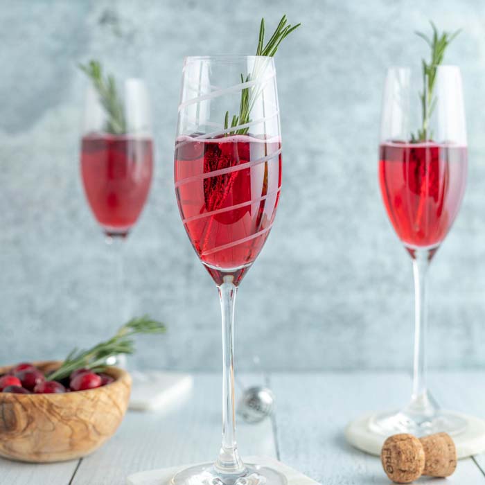 color photo of 3 bright red mocktails in flutes with an herb sprig garnish