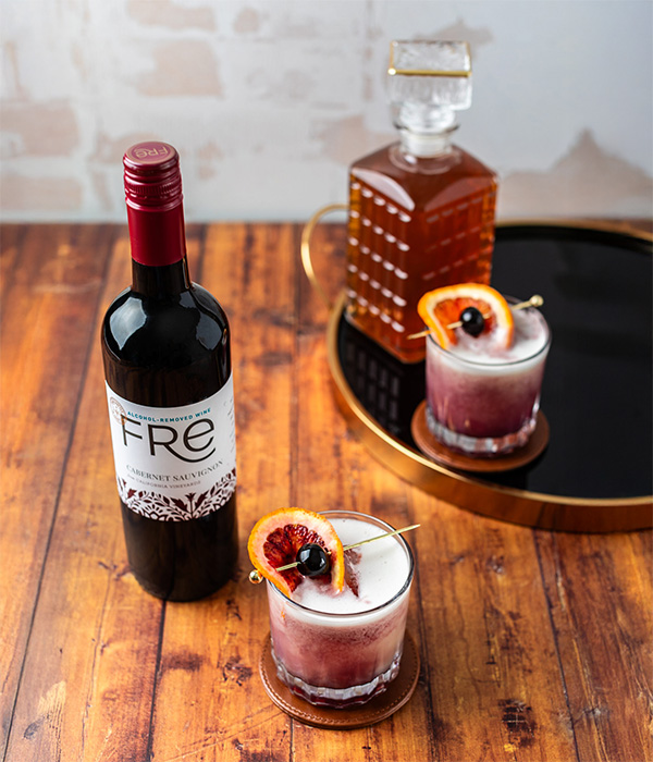 A bottle of FRE Alcohol-Removed red wine with 2 cocktails on a wood table